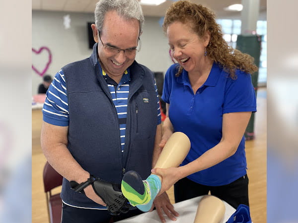 Carolyn Brown is helping a patient put a sock on a mannequin leg.