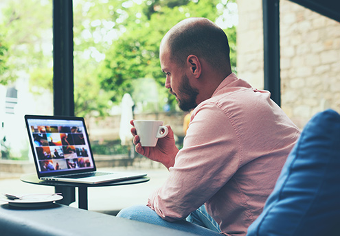 un hombre tomando café mirando la pantalla de una computadora portátil