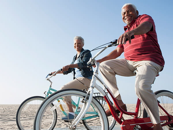 Una pareja de personas mayores de raza negra pasea en bicicleta por una playa.