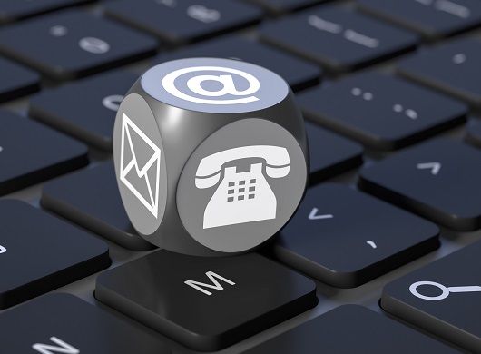 A cube with icons of a phone, @ symbol, and envelope on the visible sides is resting on a computer keyboard.