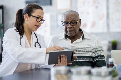 a female health care professional is showing her Black male patient information on a tablet