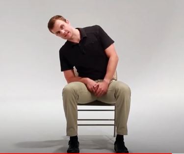 A White man is sitting in a chair leaning his head and upper body over to his right.