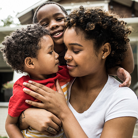 Mother and young boys hugging in front yard of home