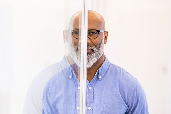 Un hombre de negocios calvo de mediana edad y su imagen reflejada en un panel de vidrio