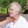 A caregiver has her hand on a senior woman's throat to assist with swallowing.