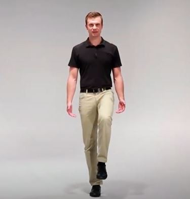 A White man is standing straight with his left knee bent and lifting his leg off the ground.