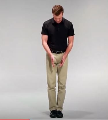 A White man is standing up straight and looking down with- his feet together.