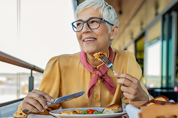 A senior woman is smiling while eating a balanced meal.