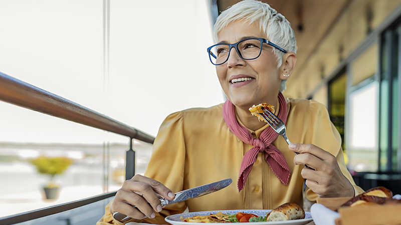 Una mujer mayor sonríe mientras come una comida equilibrada.