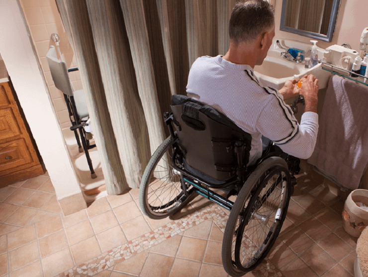 A man in a wheelchair is at the sink in his bathroom. A man in a wheelchair is at the sink in his bathroom.