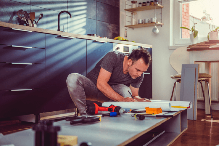 A casually-dressed man is constructing a cabinet in a kitchen. A casually-dressed man is constructing a cabinet in a kitchen.